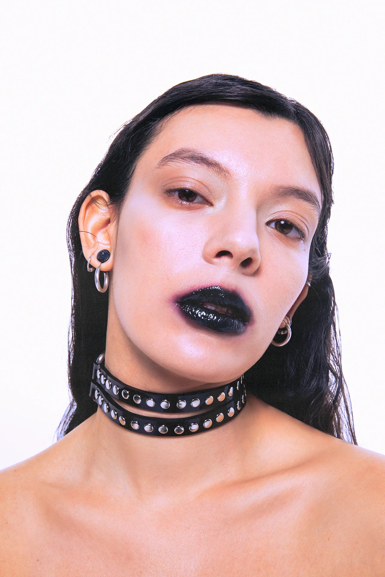 Close-up of a model wearing a double-layer black PVC choker with silver studs, styled with bold black lipstick and silver piercings – punk and fetish fashion accessory.