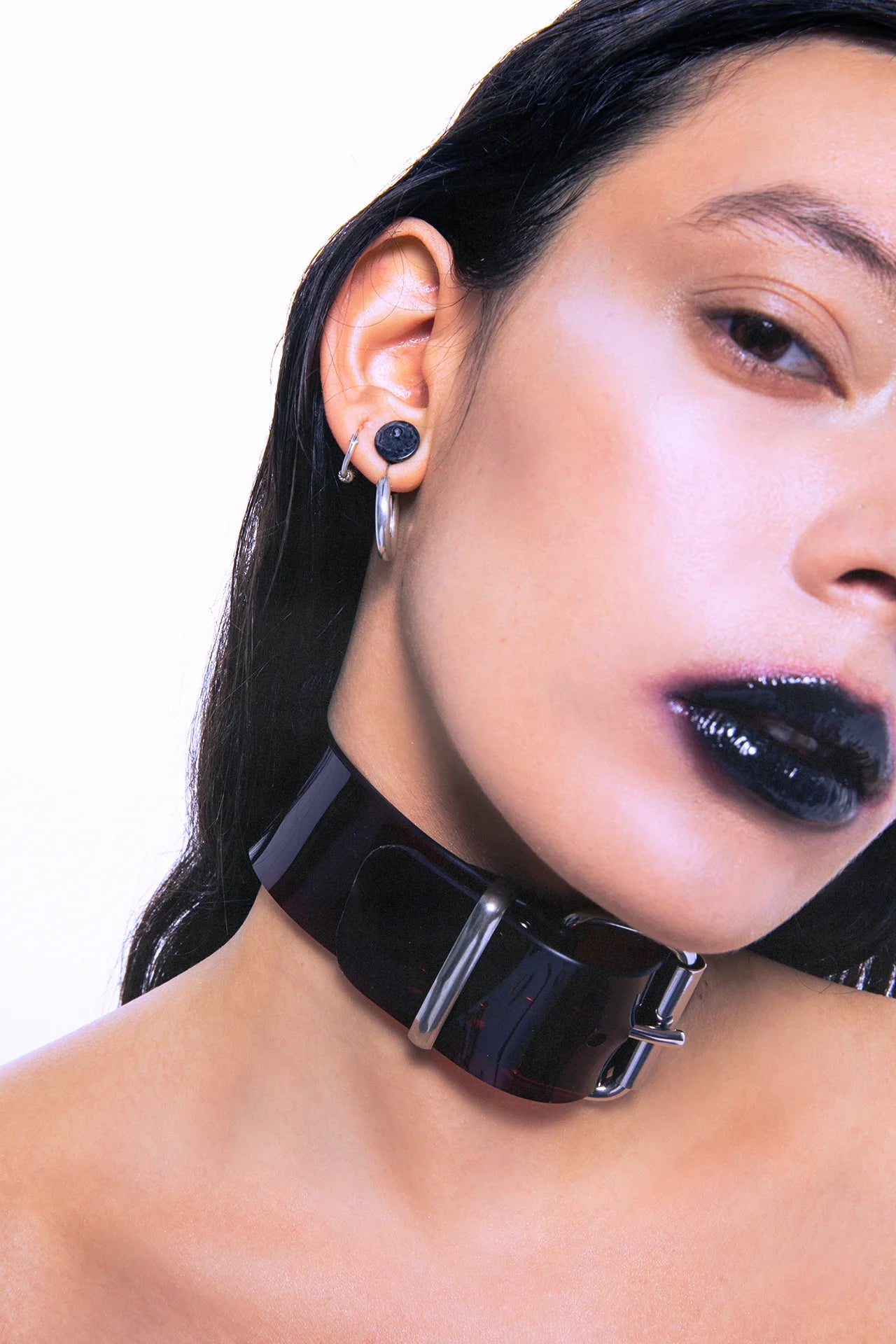 Close-up of glossy black PVC collar with silver buckle, showing high-shine material and hardware details