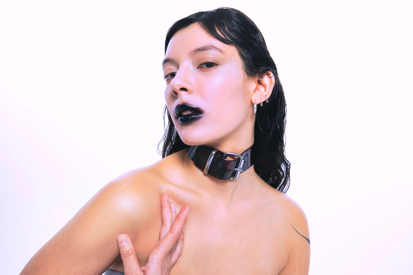 Model wearing a wide black PVC choker with a silver D-ring and buckle, styled in a bold fetish punk aesthetic